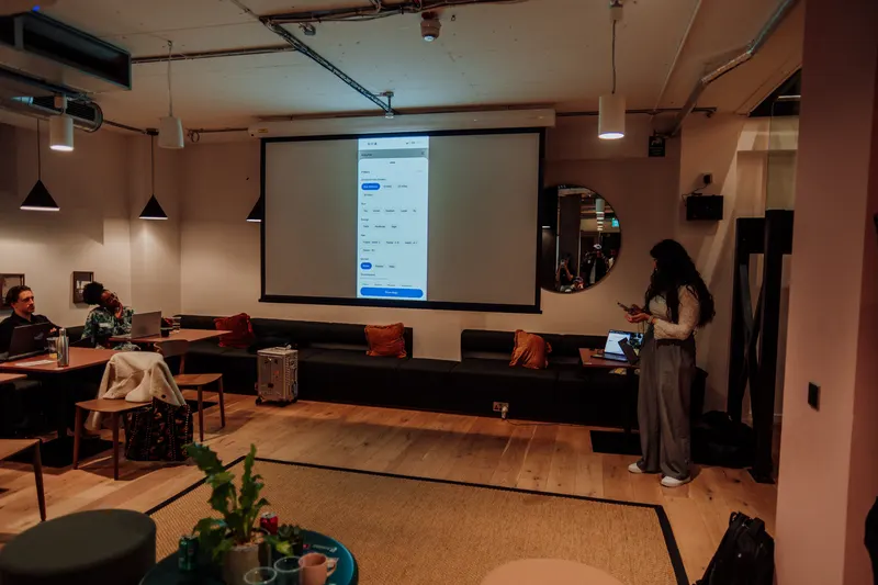A phone app demo is projected on the screen while a woman stands nearby holding her phone.