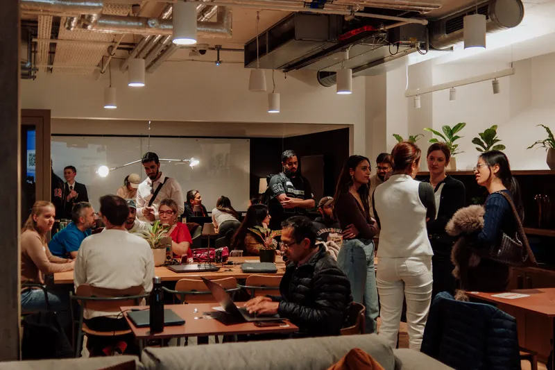 Guests stand and sit around tables across the busy event space with laptops open.