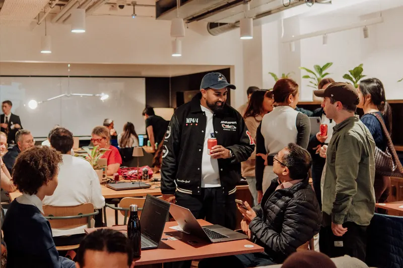 Founders sit and stand around busy tables with laptops, drinks and autumn decorations.