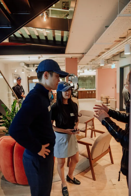 A founder in a navy cap talks with a woman beside a red armchair at Growth Night.