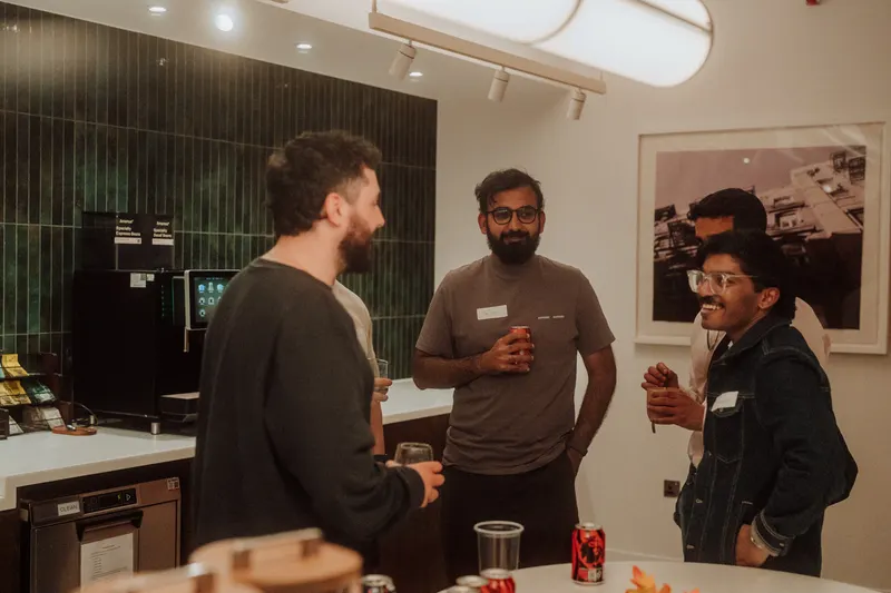 Three founders chat with drinks in hand next to a coffee machine at Growth Night.