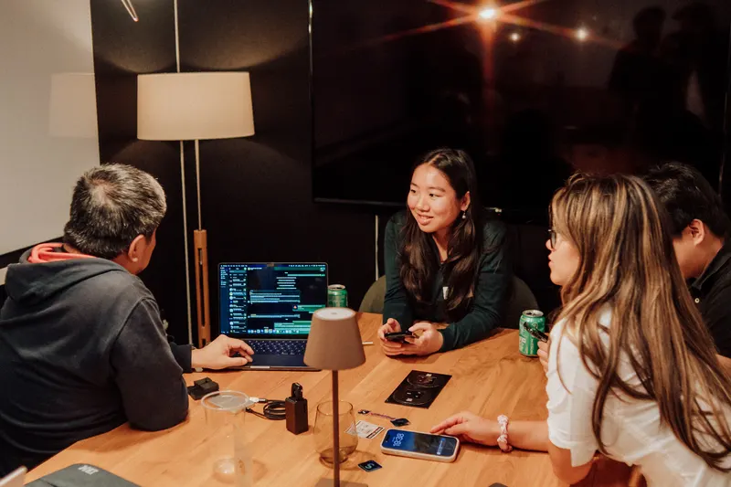 Founders sit around a table with a laptop open on code, smiling and chatting.