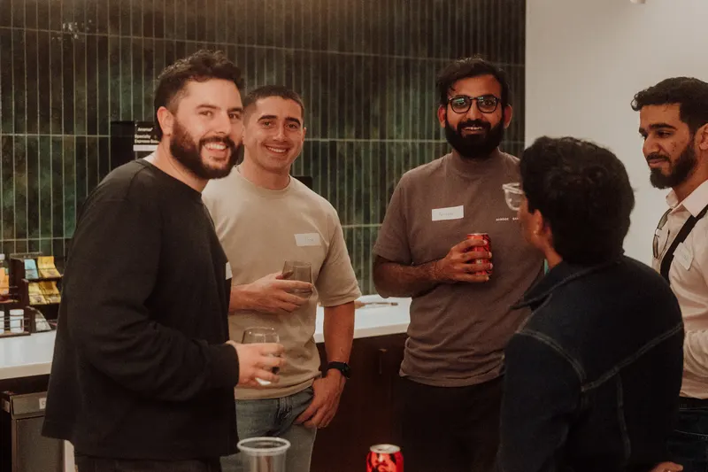 Four founders laugh and talk with drinks in hand beside a green tiled wall.