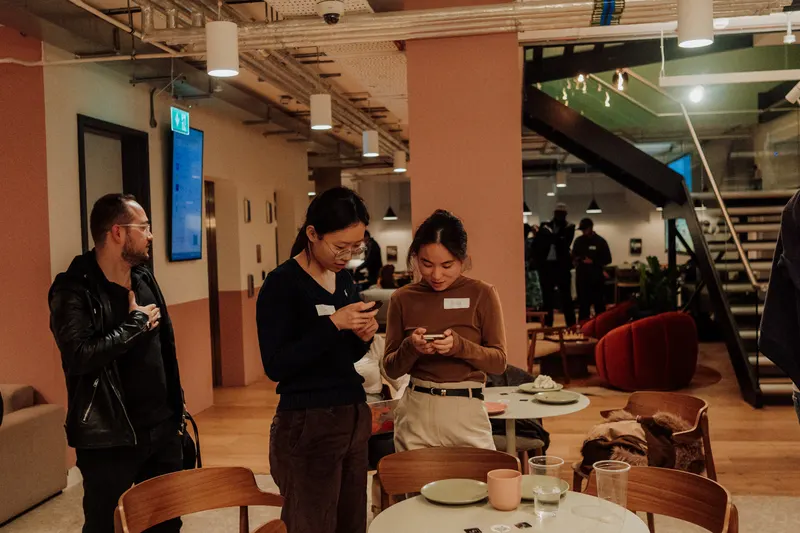 Three founders stand by a table in the venue, two looking at their phones.