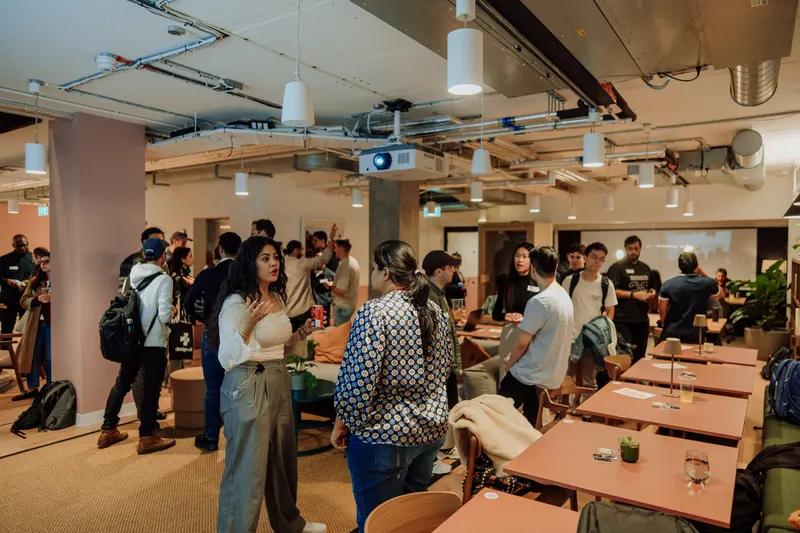 Founders mingle and talk around wooden tables in the open event space at Growth Night in London.