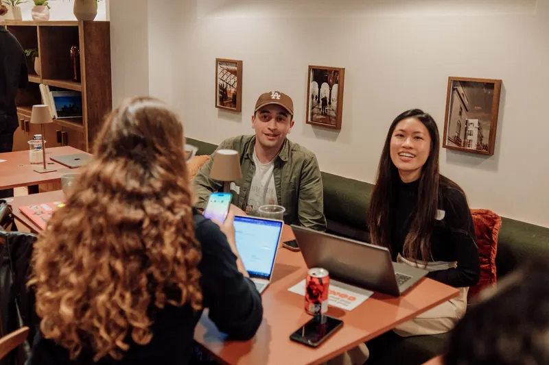 A woman with curly hair faces two founders who smile across a table of laptops.