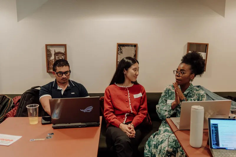 Three founders sit side by side on a bench with laptops, smiling and talking.