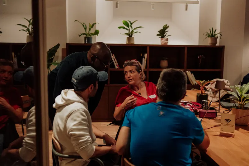 Three founders sit around a table talking while a man leans in beside them.