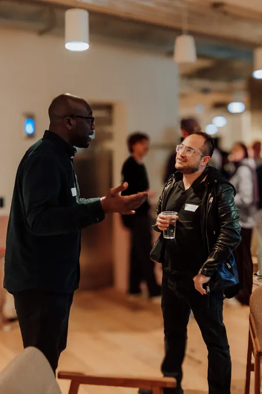 Two founders hold drinks and talk in the event space, one gesturing as he speaks.