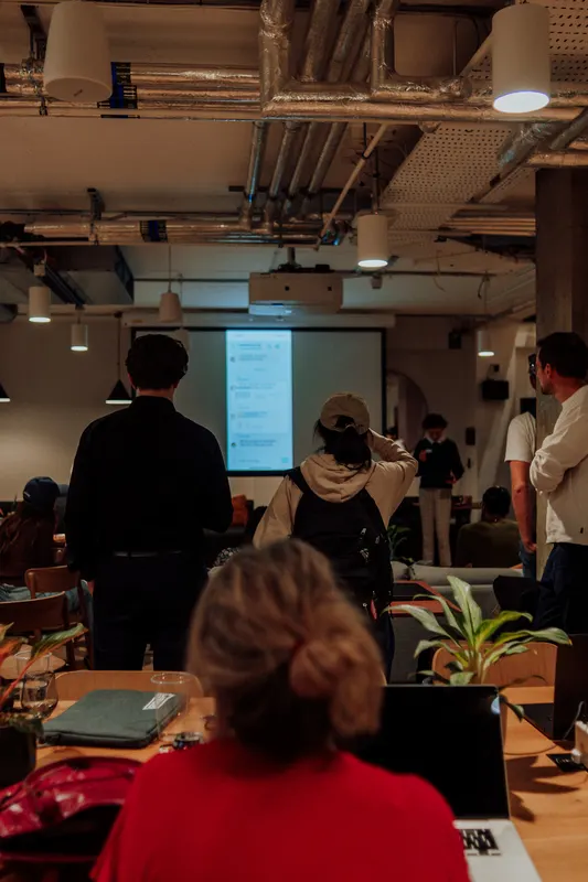Founders watch a presentation from the back of the room, with a woman in red in front.