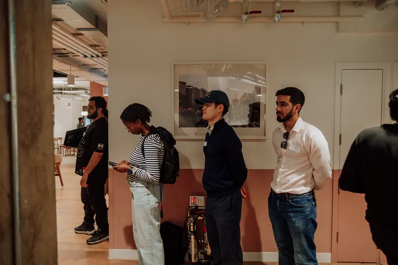 Four guests stand together by a pink wall, one looking down at a phone.