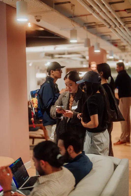 Guests stand and look at their phones while others sit on a sofa with a laptop.