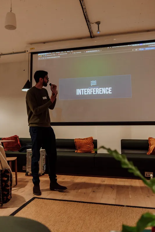 The host speaks into a microphone beside a screen showing a bold word on grey.