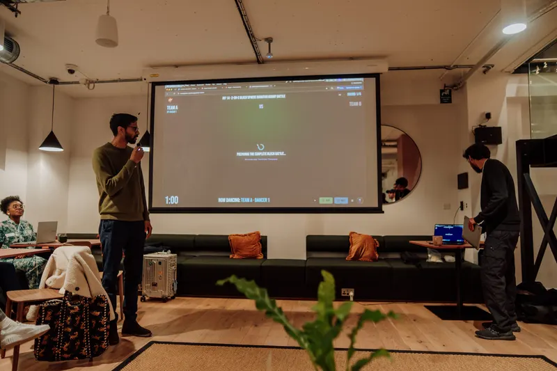 A host stands with a microphone in front of a projector screen as guests settle in.
