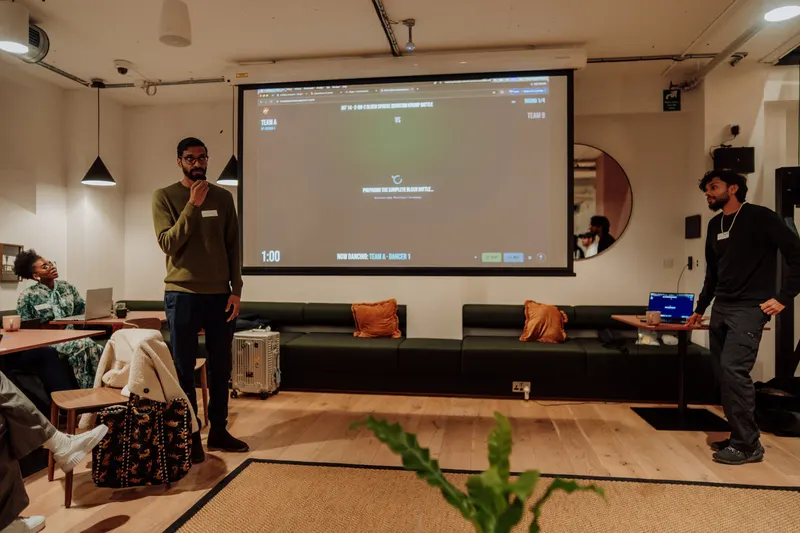 A host with a microphone talks in front of the screen while another man stands nearby.