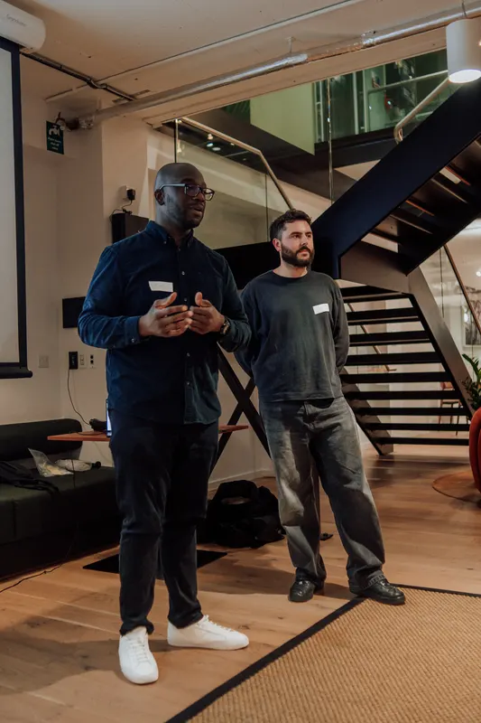 Two hosts in dark clothes stand together by the staircase at the end of Growth Night.