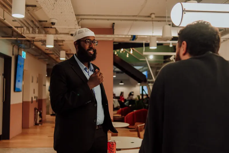 A man in a white cap and glasses laughs while another guest faces away from the camera.