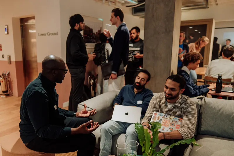 A man sits cross legged on a chair talking to two founders on a sofa.