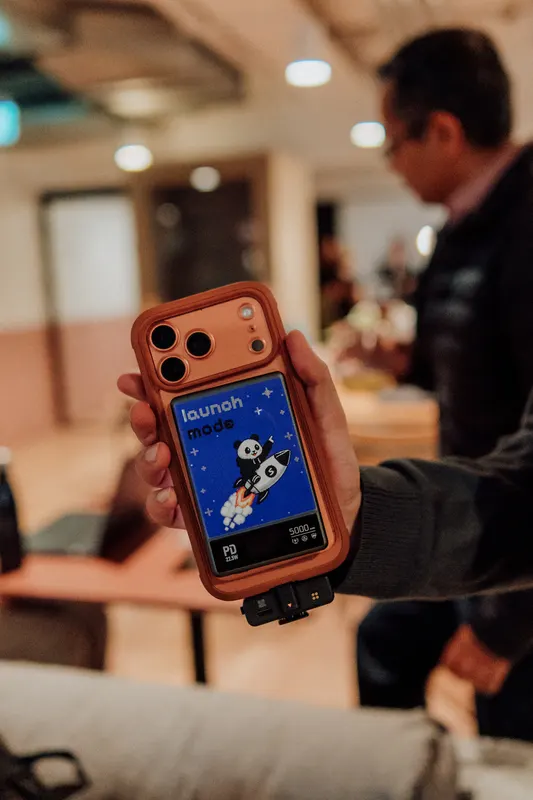 A hand holds up a phone in an orange case showing a launch screen with a rocket.