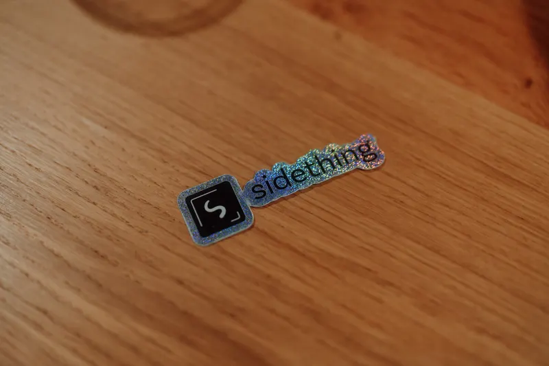 A holographic sidething sticker sits on a wooden table at Growth Night.