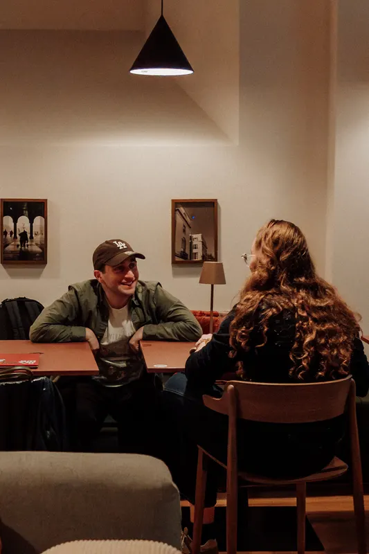 A man in a cap and a woman with long hair sit and chat at a small table.
