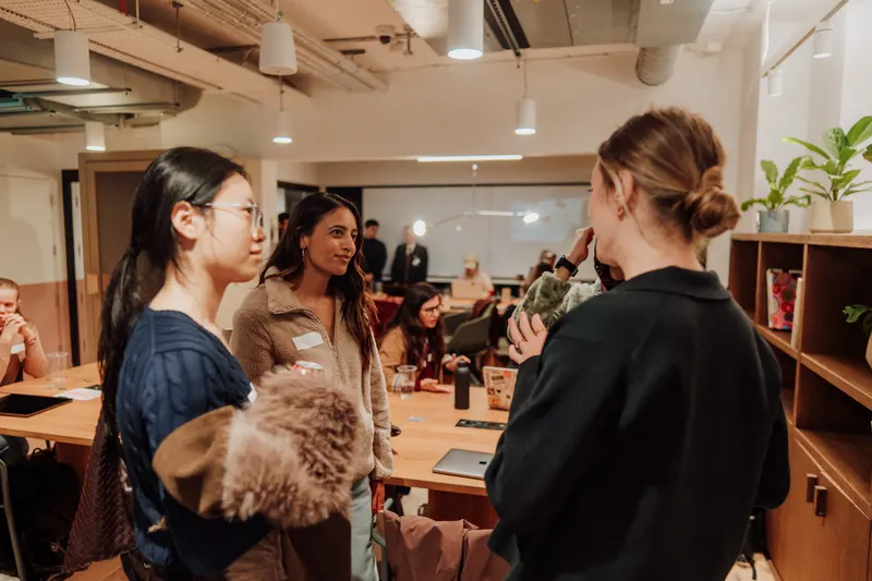 Four women stand and talk beside a table at Growth Night in London.