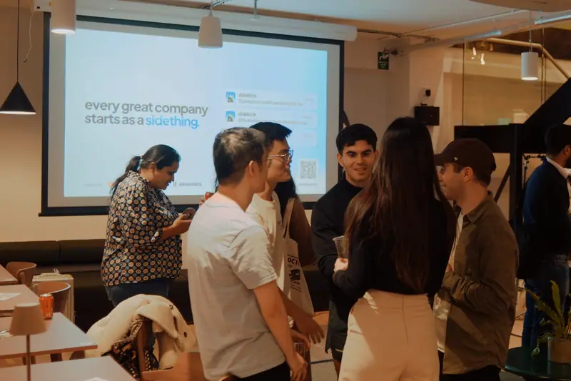 Founders chat in front of a projected slide reading every great company starts as a sidething.